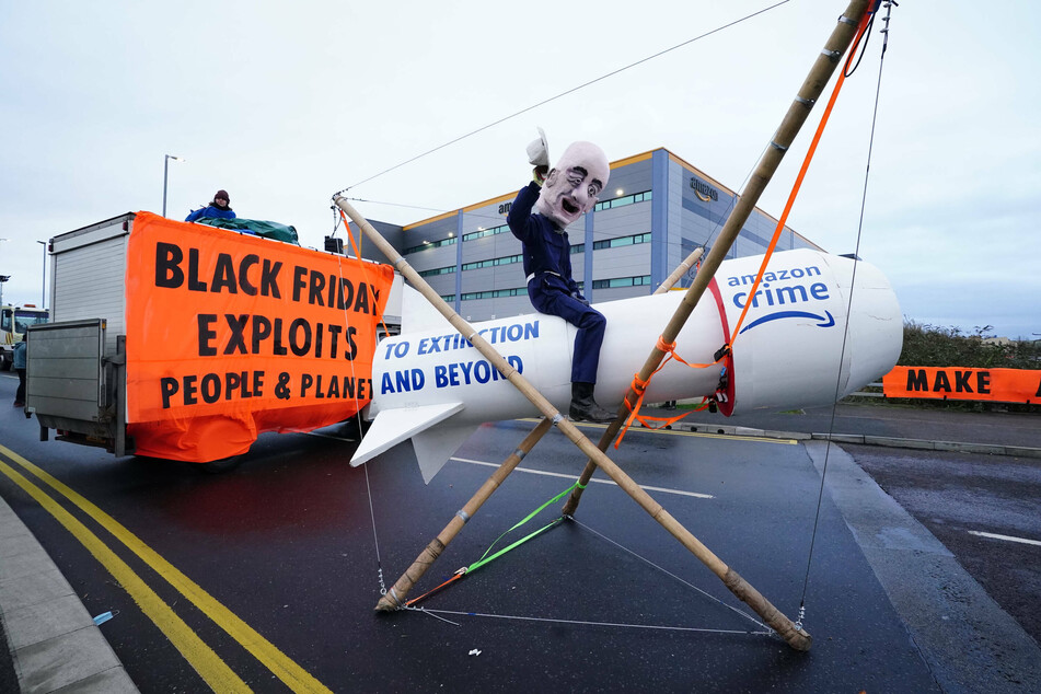An activist from Extinction Rebellion, wearing a giant Jeff Bezos head, blocks the entrance to an Amazon fulfillment center in the UK.