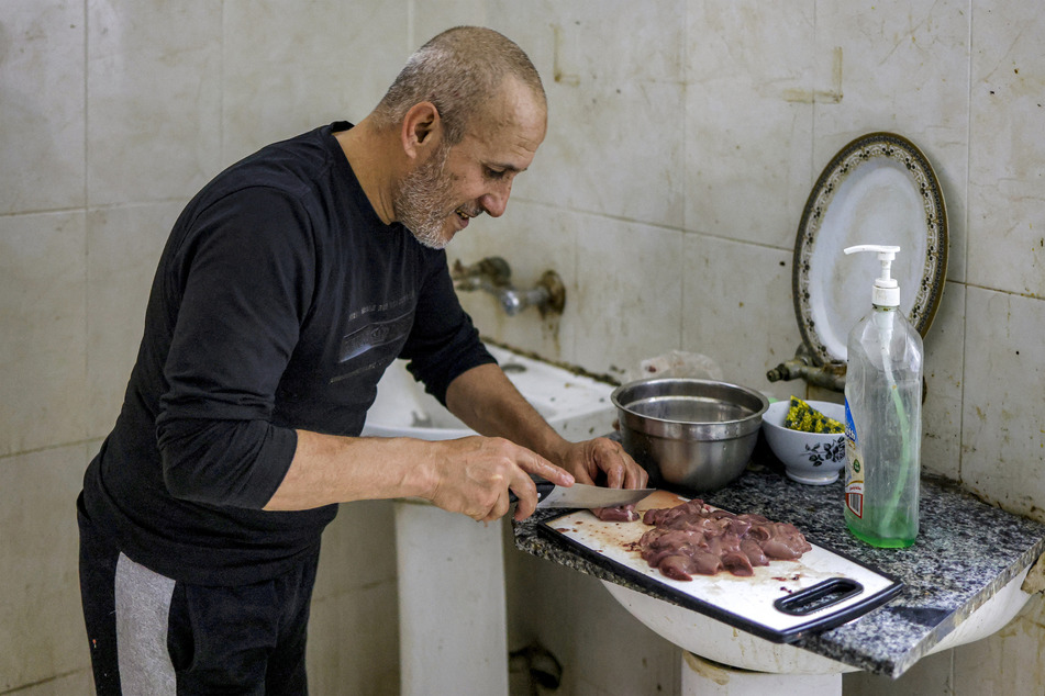 A Palestinian man from Gaza who has been stranded in the occupied West Bank cuts pieces of meat at a bathroom converted into a makeshift kitchen at Nablus Football Stadium on May 7, 2026.
