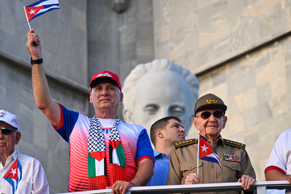 Cuba's President and First Secretary Miguel Diaz-Canel (c.) and former President Raul Castro (r.) hold Cuban flags during the commemoration of May Day at Havana's Revolution Square on May 1, 2025.