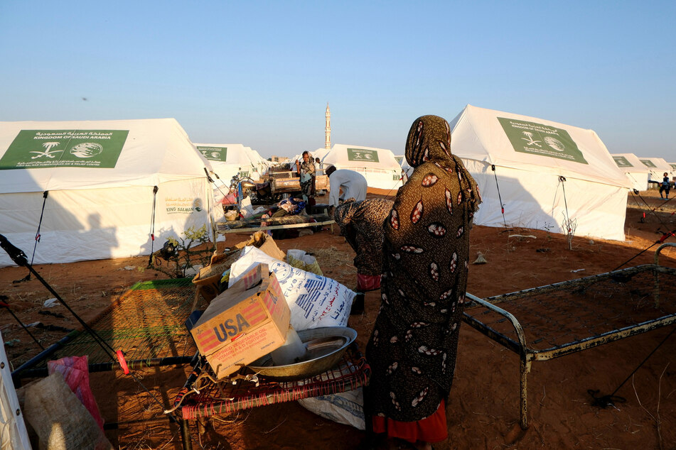 A displaced woman stands in front of an empty cardboard box labeled "USA" at a displaced persons camp in El Obeid, North Kordofan State, Sudan, on January 12, 2026.