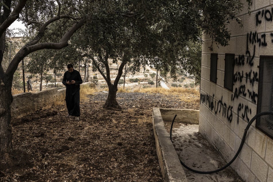 An imam walks past graffiti sprayed on the wall of a mosque following an arson attack by Israeli settlers in Mikhmas, in the Israeli-occupied West Bank, on October 14, 2026.