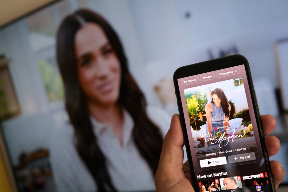 A person holds a smartphone displaying Netflix's Meghan Markle lifestyle show, "With Love, Meghan," in front of a TV screen showing footage of the show, in Los Angeles, March 4, 2025.