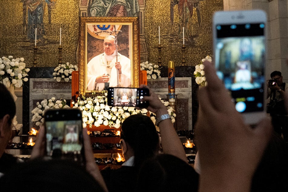 People take pictures of the image of Pope Francis displayed in the chapel of Manila Cathedral in the Philippines after the requiem mass following his death.
