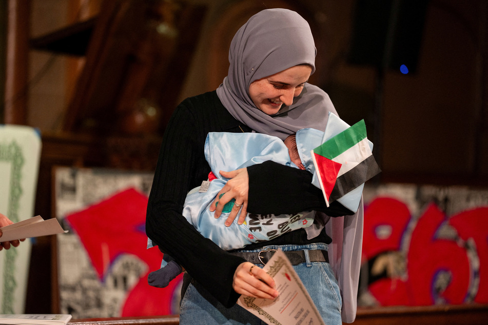 Dr. Noor Abdalla accepts an honorary diploma for her husband, Mahmoud Khalil, while holding their one-month-old baby at the People's Graduation in New York City on May 18, 2025.