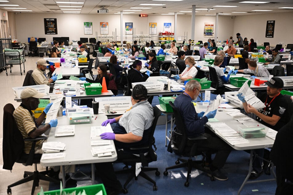Pairs of election workers from different political parties open and inspect mail-in ballot envelopes during processing on Election Day, November 5, 2024, in Phoenix, Arizona.