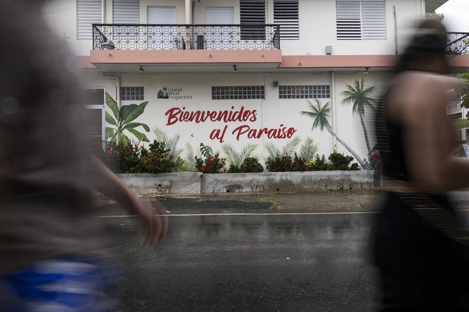 People walk past a sign that reads in English “Welcome to Paradise” in Rincon, Puerto Rico, on July 15, 2025.