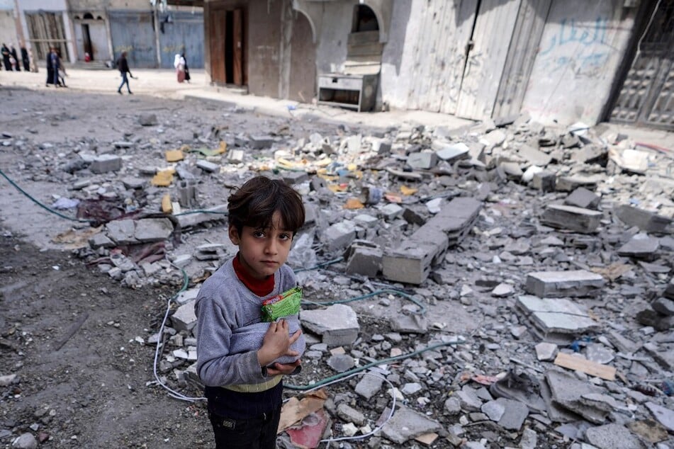 A Palestinian child holds on to food items salvaged amid the destruction caused by Israeli bombing in Bureij in the central Gaza Strip.