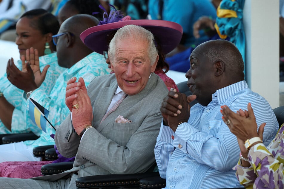 Britain's King Charles (c.) and Bahamian Prime Minister Philip Davis (r.) applaud as they sit together at a youth rally in Clifford Park in Nassau on October 27, 2026.