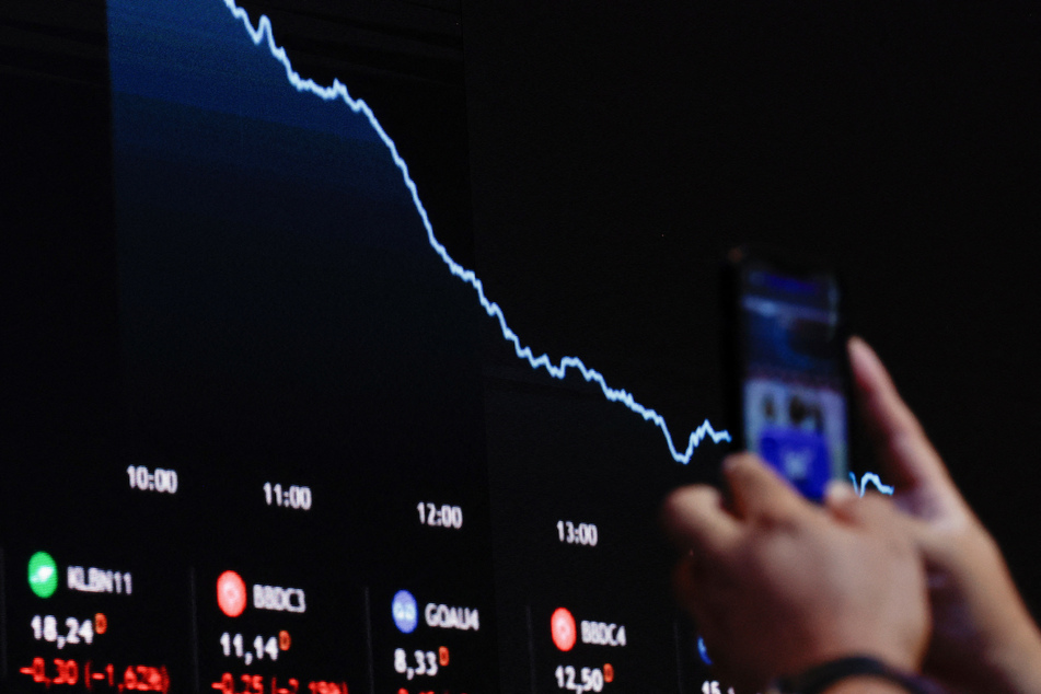 A person holds a mobile phone near an electronic board displaying information on recent fluctuations of market indices at the B3 Stock Exchange in Sao Paulo, Brazil, on April 4, 2025.