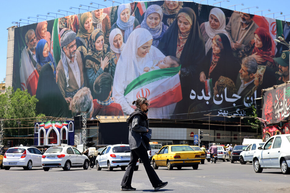 A woman crosses a street near a large political billboard along Enghelab Square in central Tehran, Iran, on May 26, 2026.