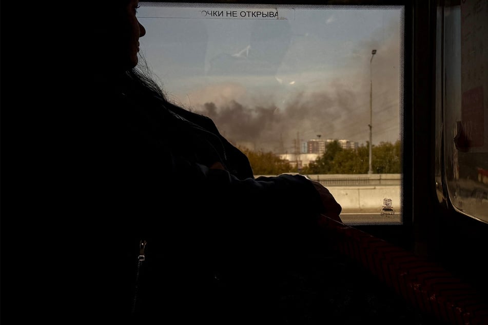 A woman rides in a bus as smoke rises from a Russian oil refinery in Moscow on September 20, after hundreds of Ukrainian drones slammed Moscow overnight.