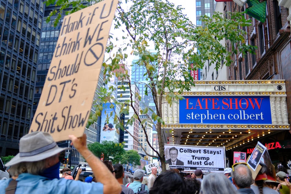 A demonstrator holds a sign reading "Honk if U think WE Should [cancel] DT's S*** Show" outside the Ed Sullivan Theater in New York City.