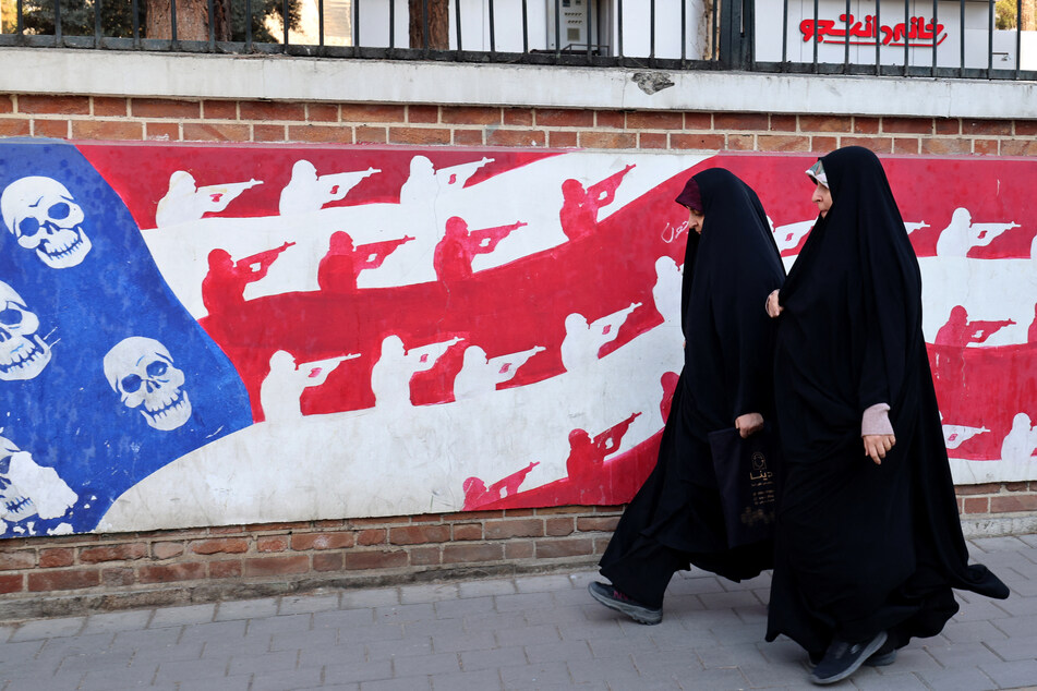 Women walk past a mural painted on the outer walls of the former US embassy in Tehran, colloquially referred to as the "Spy Den," on February 1, 2026.