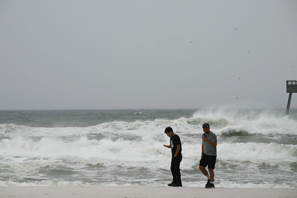 People walk on the beach in Navarre, Florida, on October 9, 2026, before Hurricane Isaias is due to make landfall. The hurricane rapidly intensified into a major Category 3 storm, triggering mandatory evacuations as it barrels towards the Gulf Coast with a projected 11 PM landfall.