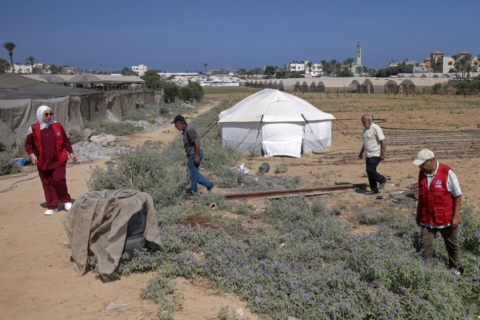 Amani Al-Naouq (l.), spokesperson for the International Committee of the Red Cross in Gaza, agricultural engineer Abdel Moneim Ahmed (second l.), and ICRC economic security officer Osama Al-Mukhalalati (r.) walk through a field near the Al Qarara Seed Bank in Deir el-Balah on August 11, 2026.