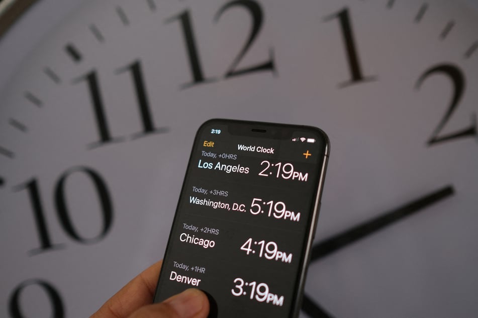 This illustration photo shows a clock in the background of a smartphone showing the time after daylight saving time was implemented in Los Angeles, California, on March 15, 2022.
