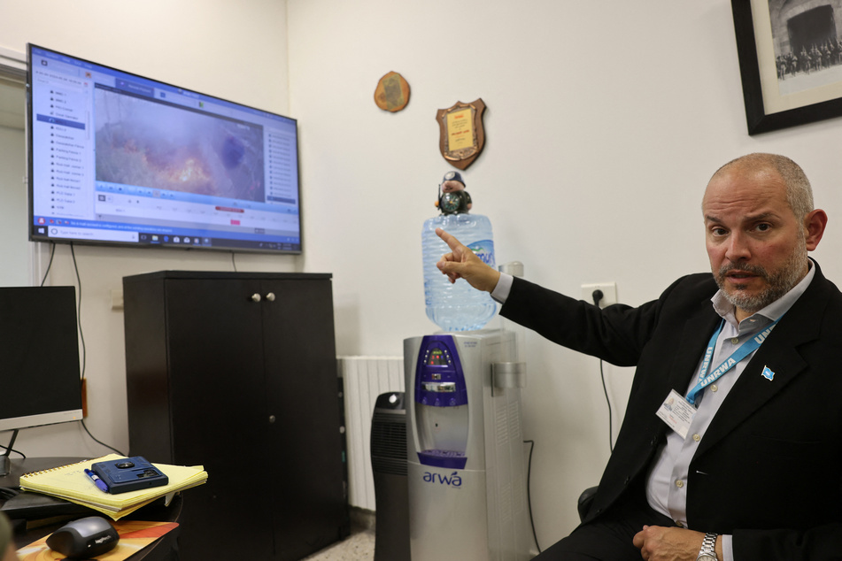UNRWA Affairs Director in the West Bank Adam Bouloukos points to CCTV footage showing a fire burning on the perimeter.