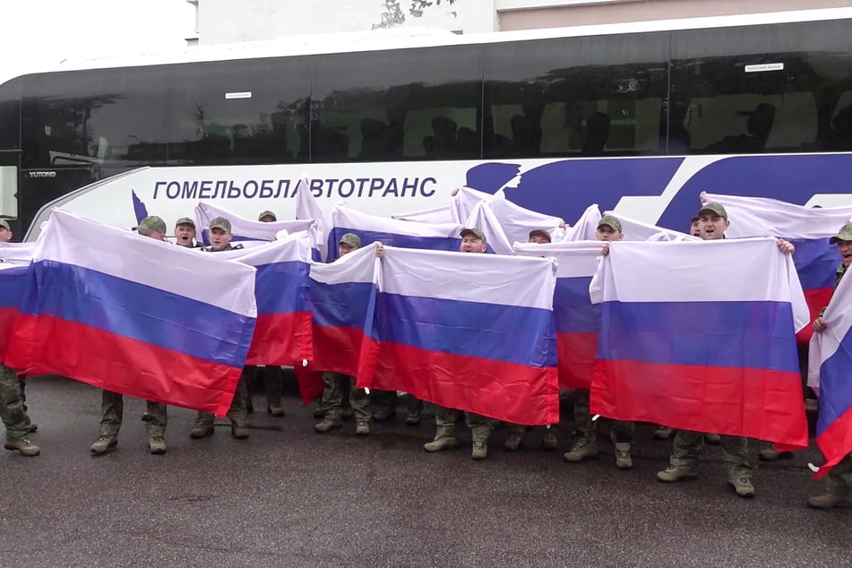 Russian prisoners of war pose with flags in front of a bus following a POW exchange at an undisclosed location in Belarus on May 15, 2026.