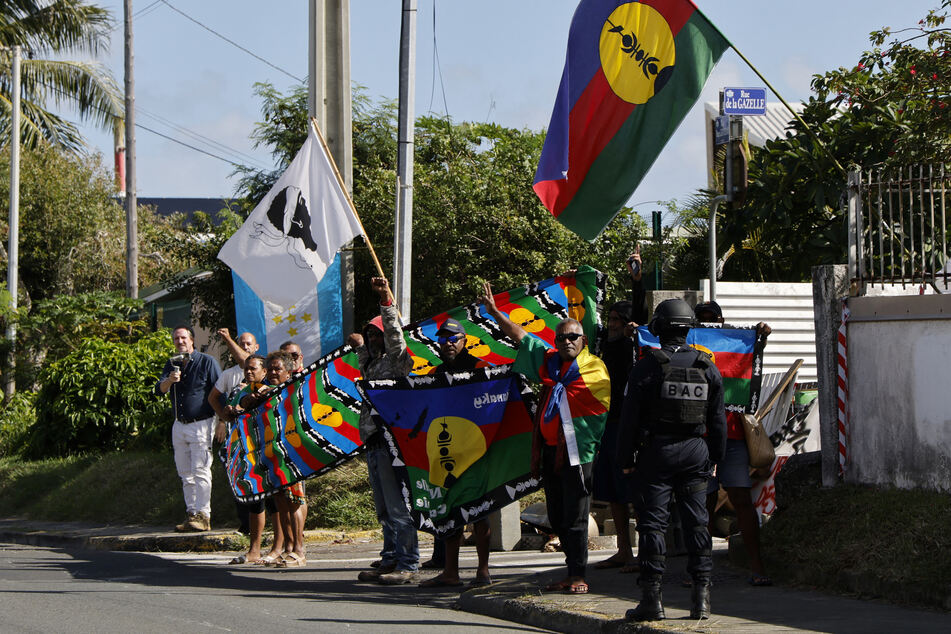 People demonstrate as French President Emmanuel Macron's motorcade drives past in Noumea, New Caledonia.
