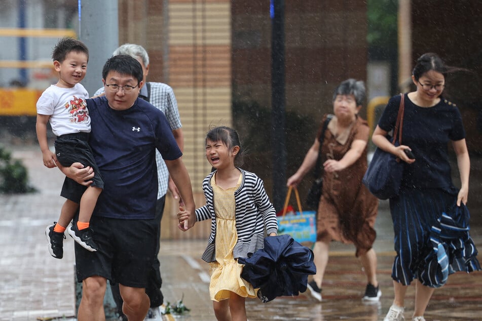 People brave the heavy wind and rain from Typhoon Noul as they cross a street in Hong Kong on July 26, 2026.