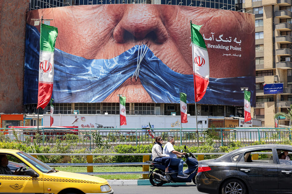 People drive past a political billboard featuring US President Donald Trump and the Strait of Hormuz along Valiasr Square in Tehran on May 26, 2026.
