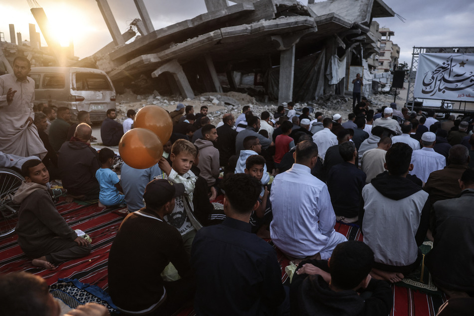 A boy holding balloons stands among Palestinians gathering on a heavily damaged street to perform morning prayers marking the start of Eid al-Adha, the Feast of Sacrifice, in Khan Younis in the southern Gaza Strip on May 27, 2026.