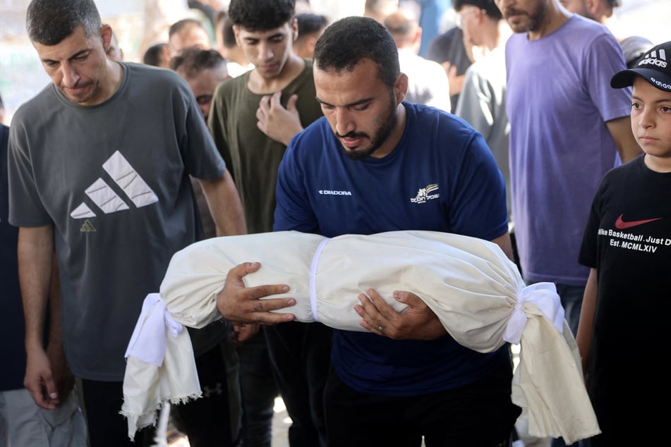 A mourner carries the shrouded body of an infant killed in an overnight Israeli airstrike the Al-Shifa Hospital in Gaza City on August 2, 2026.