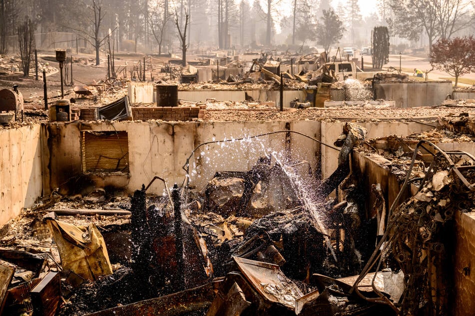 Water sprays from a broken pipe at a burned home during the Old Trails Fire in Spokane, Washington, on Tuesday.