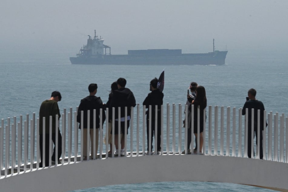 Chinese tourists watch a cargo ship sailing through the Taiwan Strait, on the coast of Pingtan island, the closest point in China to Taiwan, in southeast China's Fujian province on April 16, 2023.