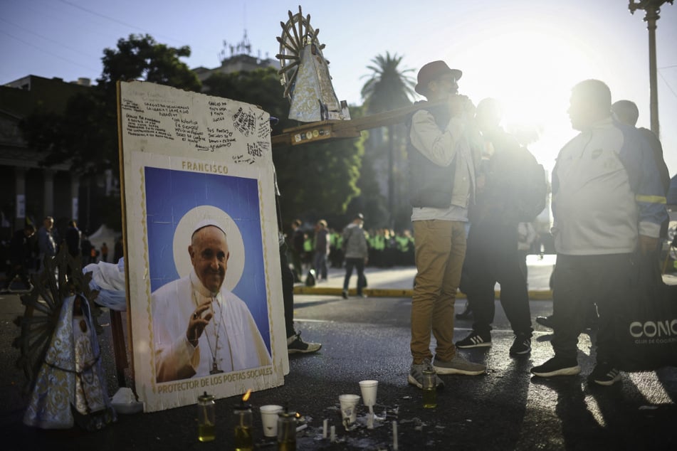 People stand next to a picture of the late Pope Francis on the day of his funeral in Buenos Aires, Argentina.