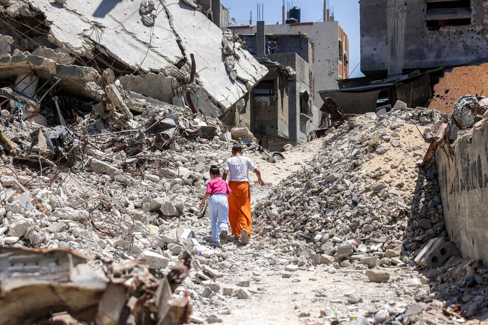 Two girls walk past the rubble of collapsed buildings in Khan Younis in the southern Gaza Strip on August 25, 2026.