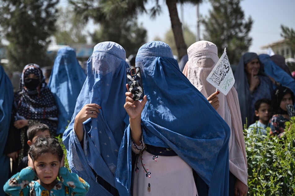 An Afghan woman uses a smartphone to take videos during celebrations to mark the fifth anniversary of Taliban governments's return to power, along a street in Kandahar on August 15, 2026.