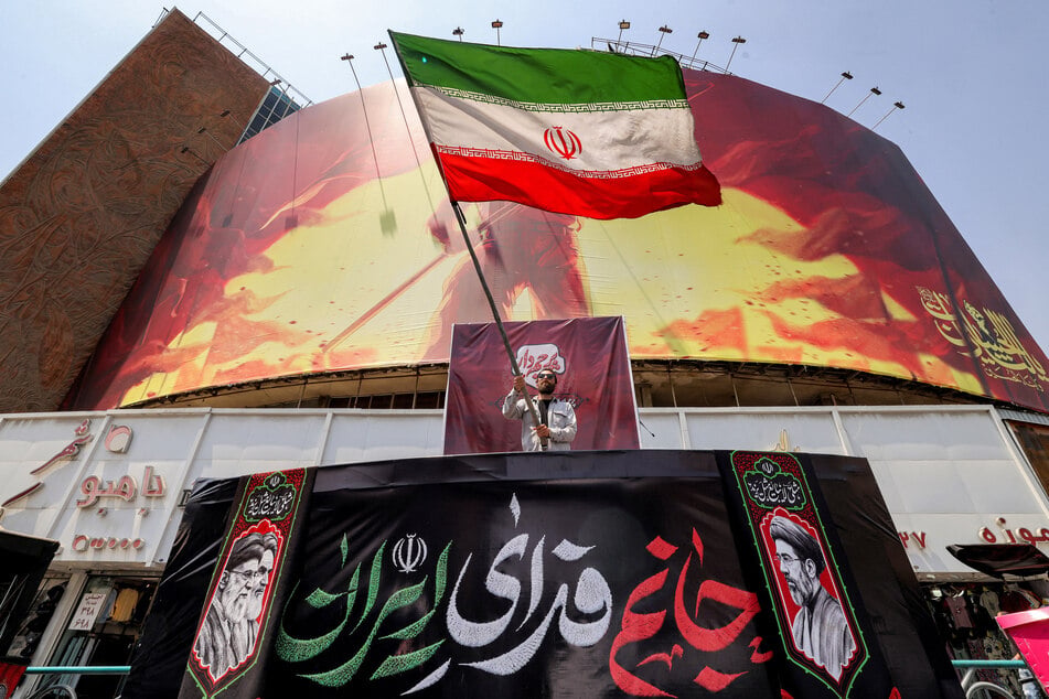 A man waves an Iranian flag before a political billboard at Valiasr Square in central Tehran on August 8, 2026.