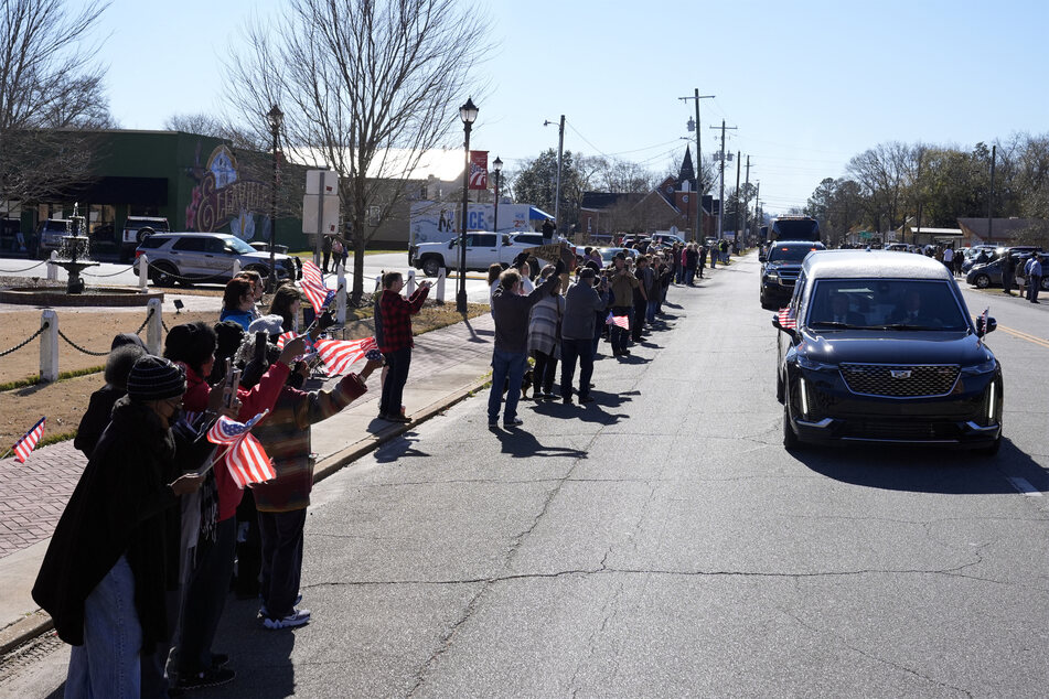 People watch as the hearse containing the flag-draped casket of former President Jimmy Carter passes by on Saturday in Ellaville, Georgia.