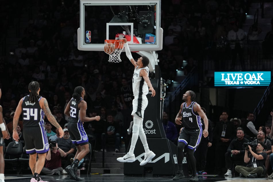 San Antonio Spurs forward Victor Wembanyama dunks in front of Sacramento Kings forwards Jonathan Mogbo and Precious Achiuwa in the first half at Frost Bank Center.