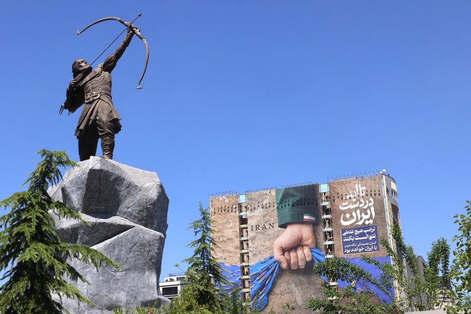 A billboard on the facade of a building depicting the Strait of Hormuz with a caption in Persian reading "Forever in Iran’s Hand" is pictured near a sculpture of Arash the Archer, a legendary figure from Persian mythology, in Vanak Square in Tehran on May 25, 2026.