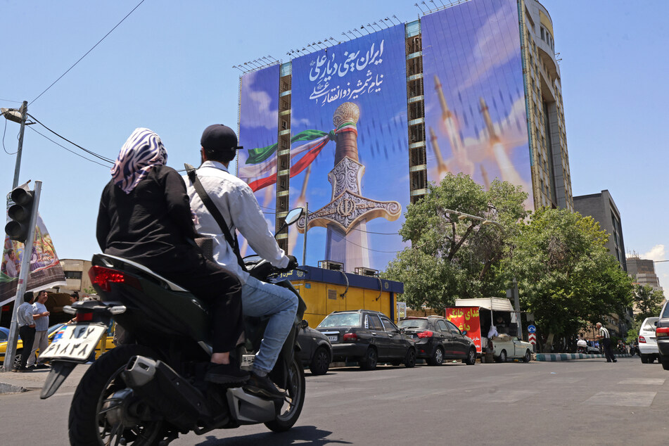 Motorists ride past a giant banner depicting Iranian missiles and a sword belonging to Imam Ali, the first Imam of the Shiites, at the Vanak Square in Tehran on June 10, 2026.