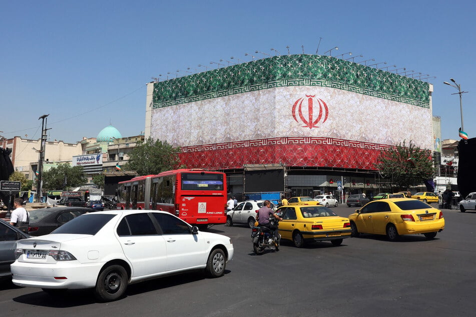 Traffic moves past the Iranian national flag displayed on a building at Enghelab square in Tehran on June 14, 2026.
