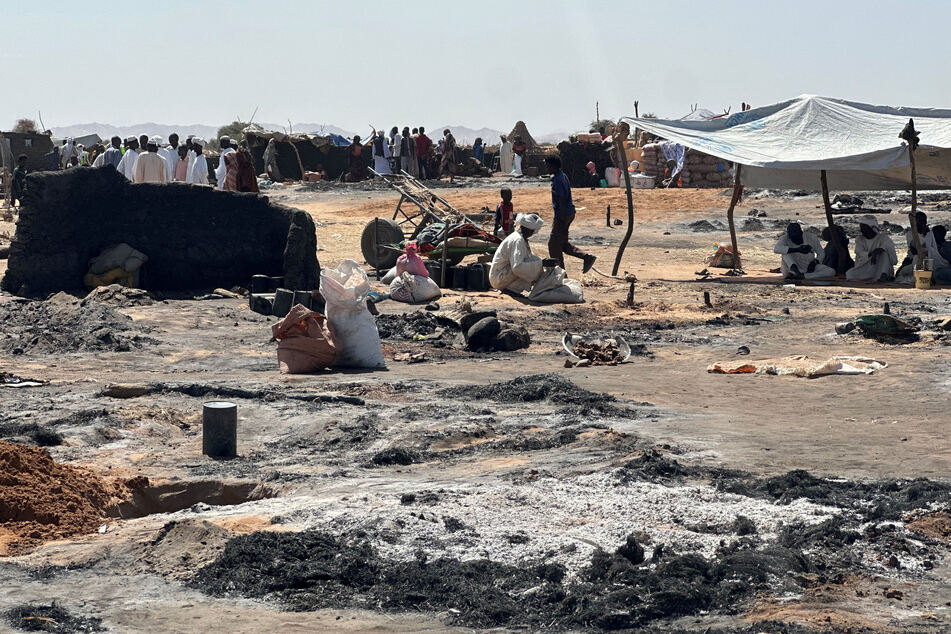 Displaced Sudanese people who left El-Fasher after its fall, sit in the shade in Tawila amid the remains of a fire that broke out in the camp on February 11, 2026.