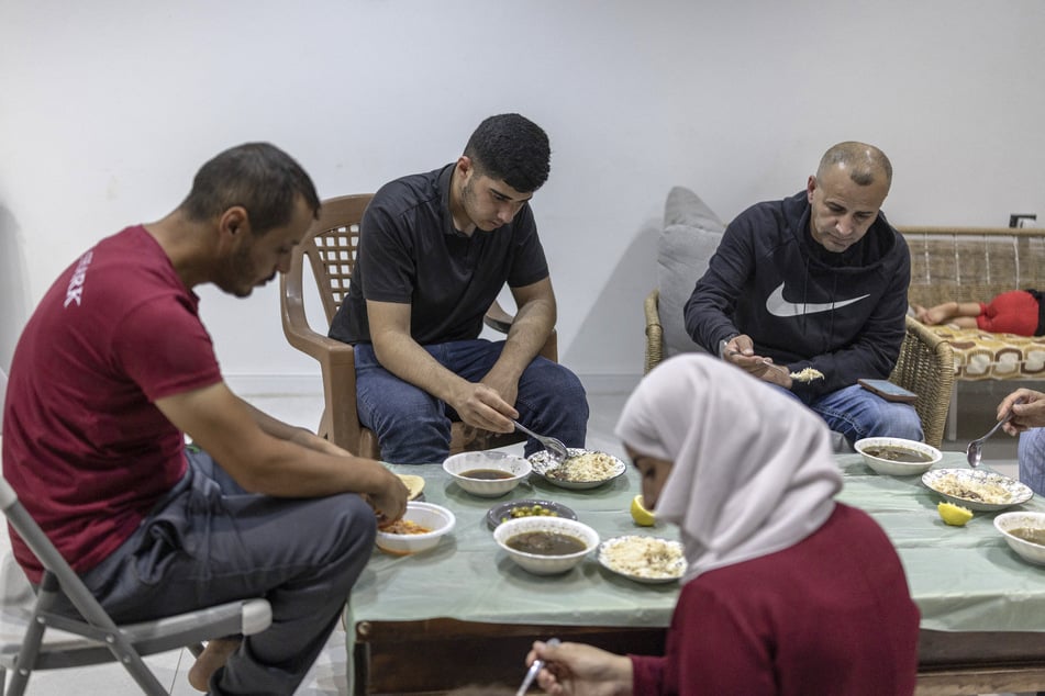 Louai Abu Ridi (r.) shares an evening meal with his family members at his besieged home in Qusra on August 18, 2026.