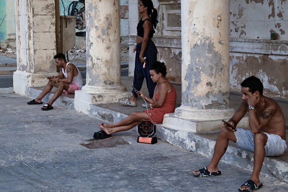 People use their mobile phones on a street in Havana during a nationwide power cut on August 3, 2026.