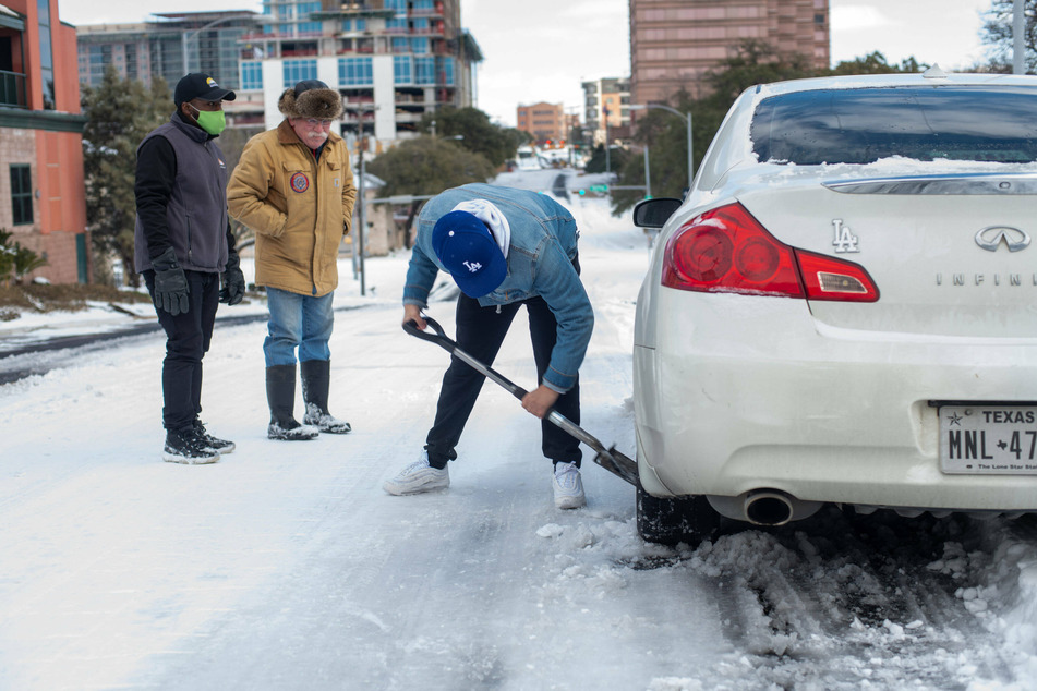 Austin, Texas: a man shovels ice from underneath his car tires after getting stuck in thick snow.