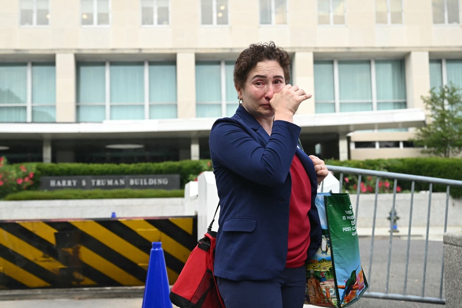 A laid-off employee fights back tears while carrying a box of office belongings as she leaves the US State Department in Washington, DC, on Friday.