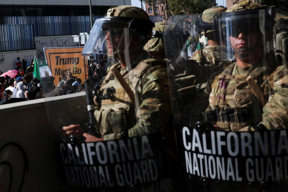 Members of the California National Guard stand in a line, blocking an entrance to the Federal Building in Los Angeles, as immigrants' rights demonstrators gather nearby on June 9, 2025.