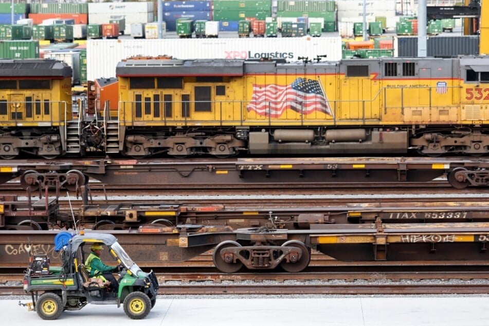 A worker drives near freight trains and shipping containers in a Union Pacific Intermodal Terminal rail yard in Los Angeles, California.