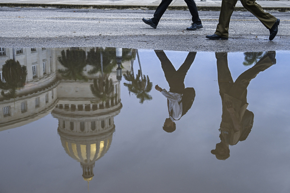 The reflection of pedestrians walking past the Havana Capitol is seen in a puddle in Cuba on July 11, 2026.
