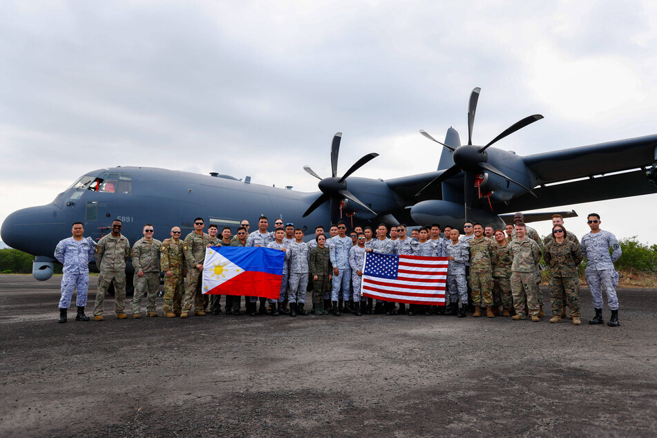 Filipino and American soldiers pose for group photos with their respective flags in front of an AC-130J military aircraft as part of the Balikatan Exercises.