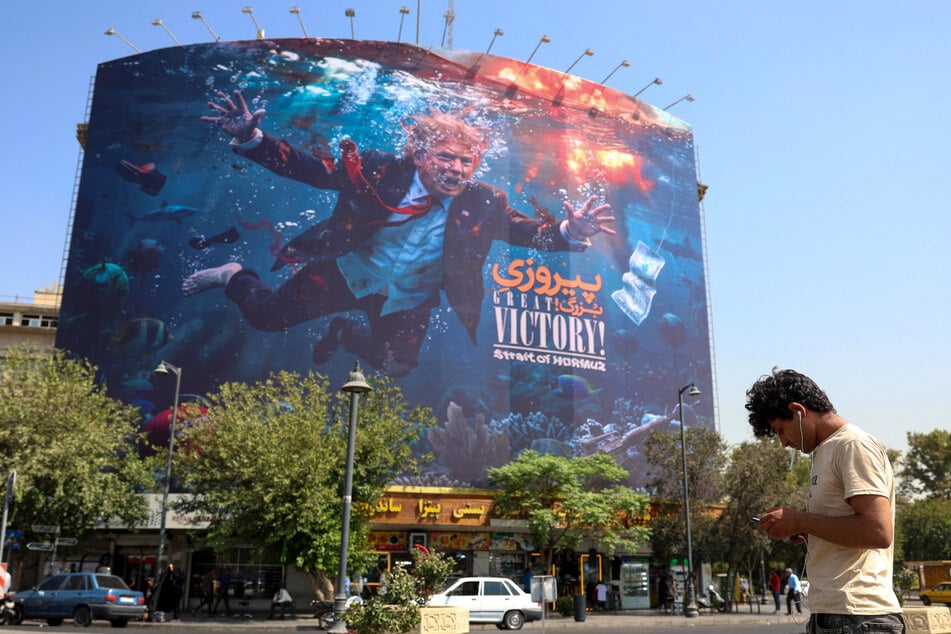 A man uses his cellphone as he stands in front of an anti-US billboard in Tehran, Iran, on August 24, 2026.