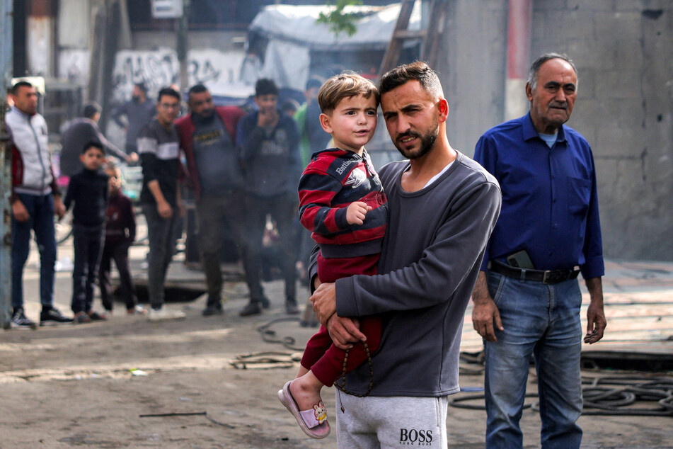 A man carrying a child stands with others as they inspect the damage at the Jabalia municipality garage, which was hit by Israeli bombardment in the northern Gaza Strip on April 22, 2025.