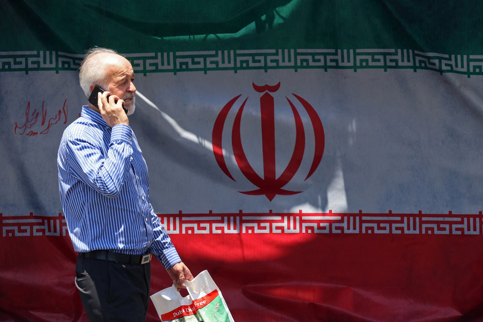A man walks past Iran's national flag at the Vanak Square in Tehran on June 10, 2026.